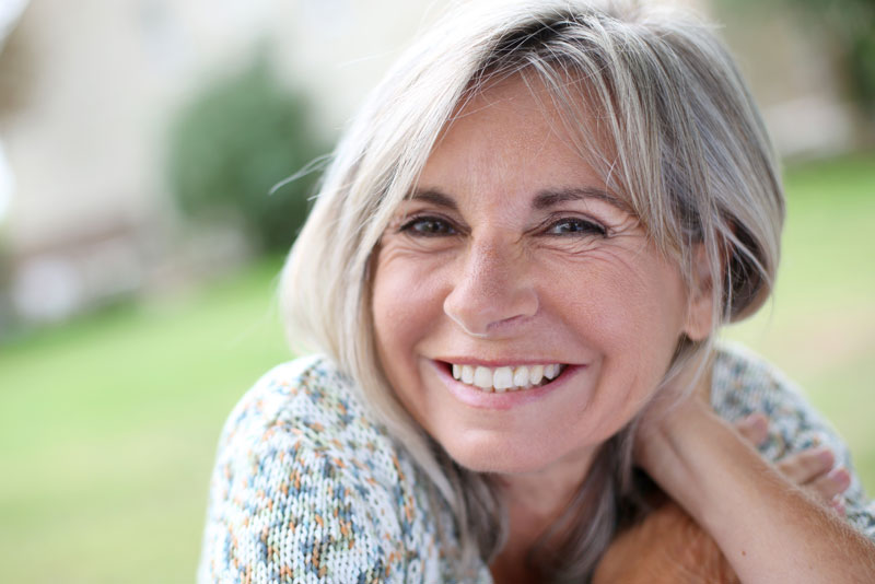 an older dental patient smiling because she got treated with the Snap-On-Smile procedure.